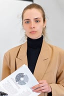 Young woman with hair tied back in a camel blazer holding documents