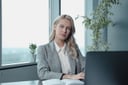 Blonde businesswoman in a grey blazer at her desk in a bright office