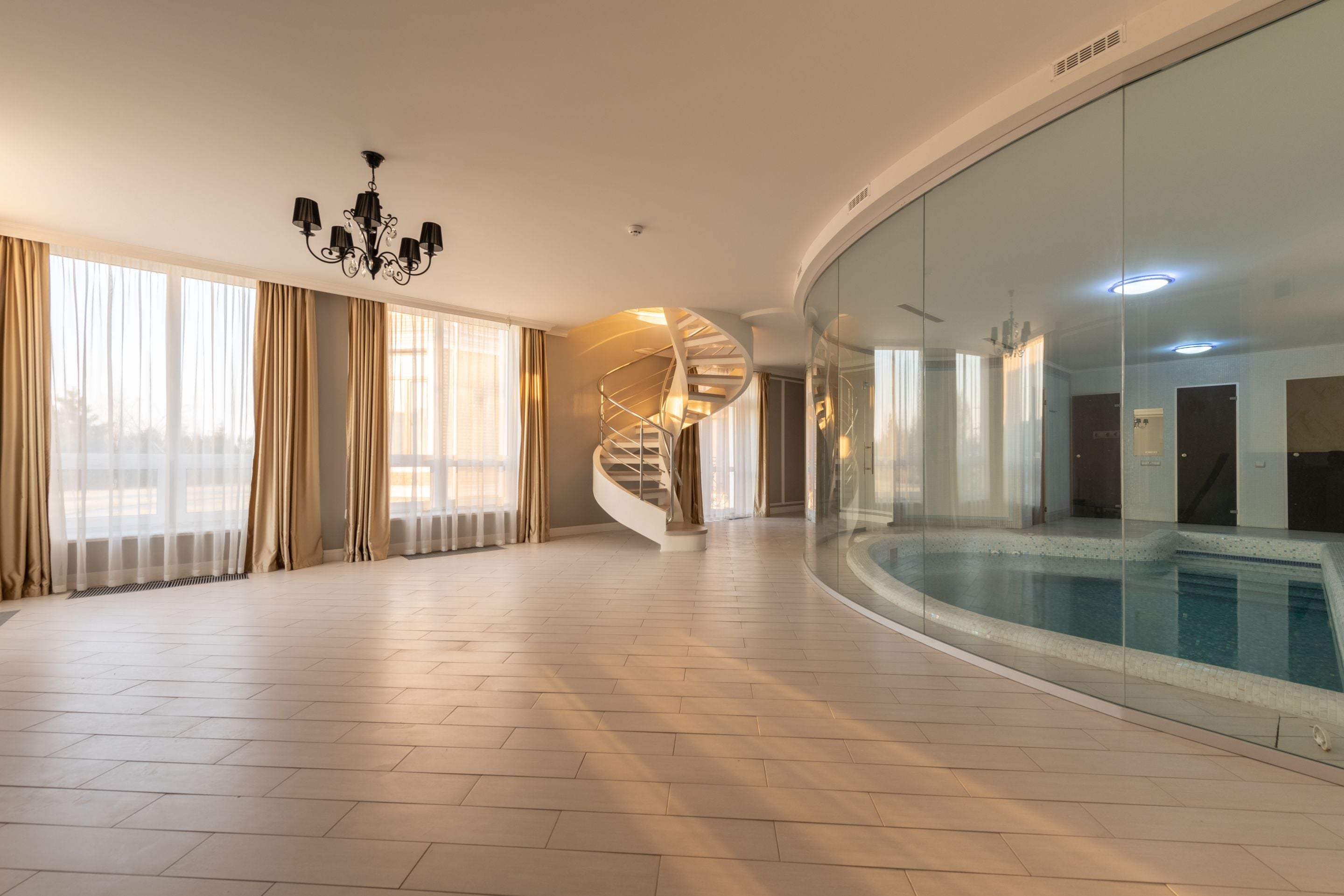 Indoor swimming pool behind a curved glass wall in a spacious hall with chandelier