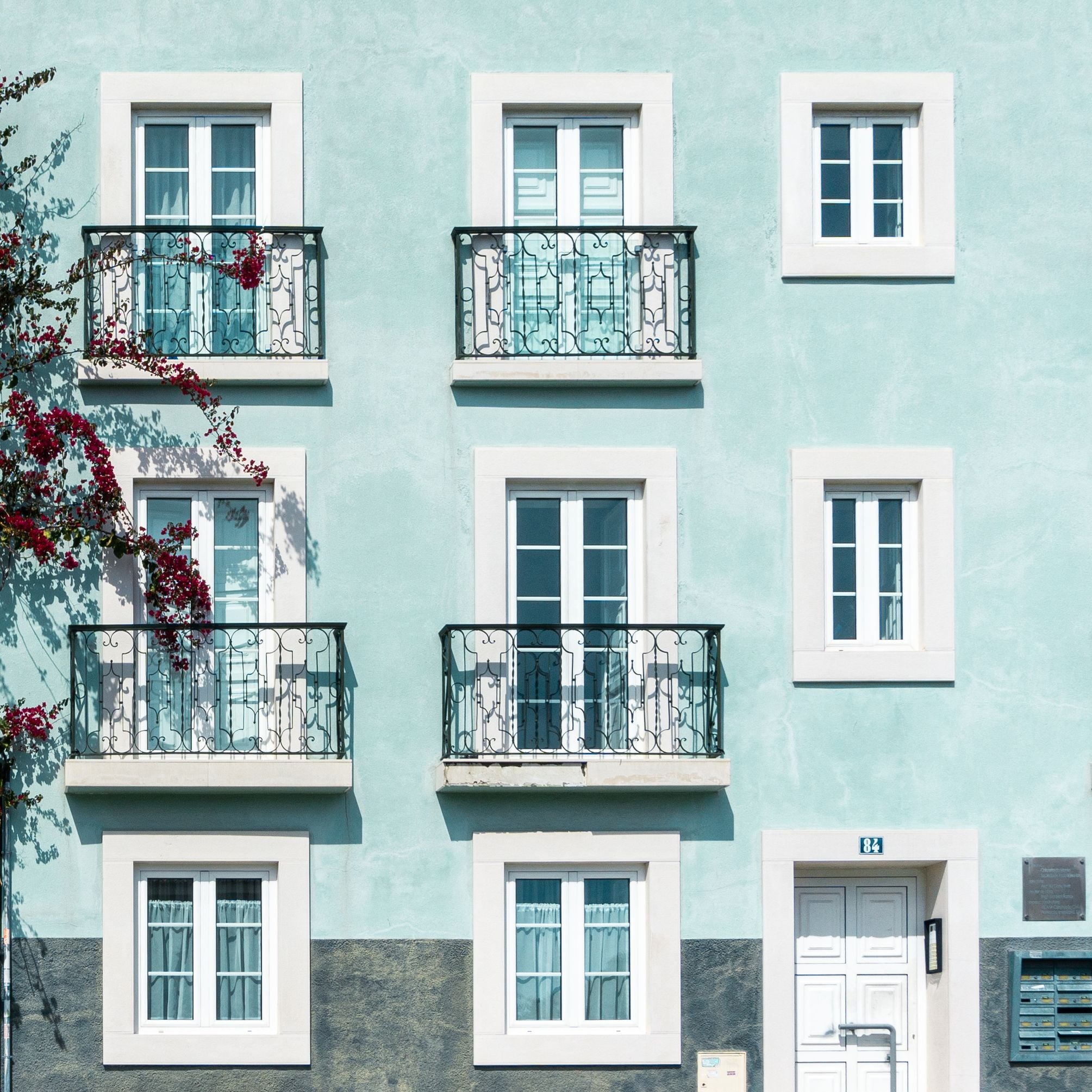 Pale blue apartment facade with white-framed windows and iron balconies