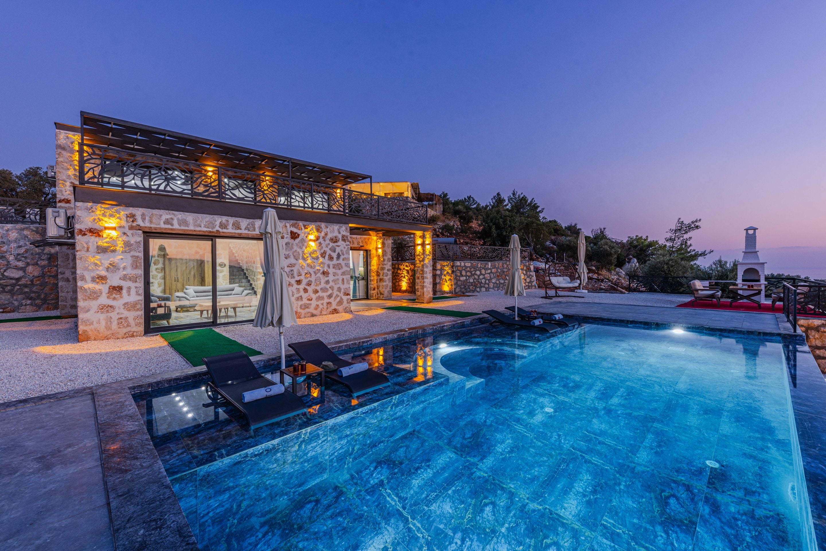 Stone and glass villa with illuminated infinity pool at twilight with purple sky