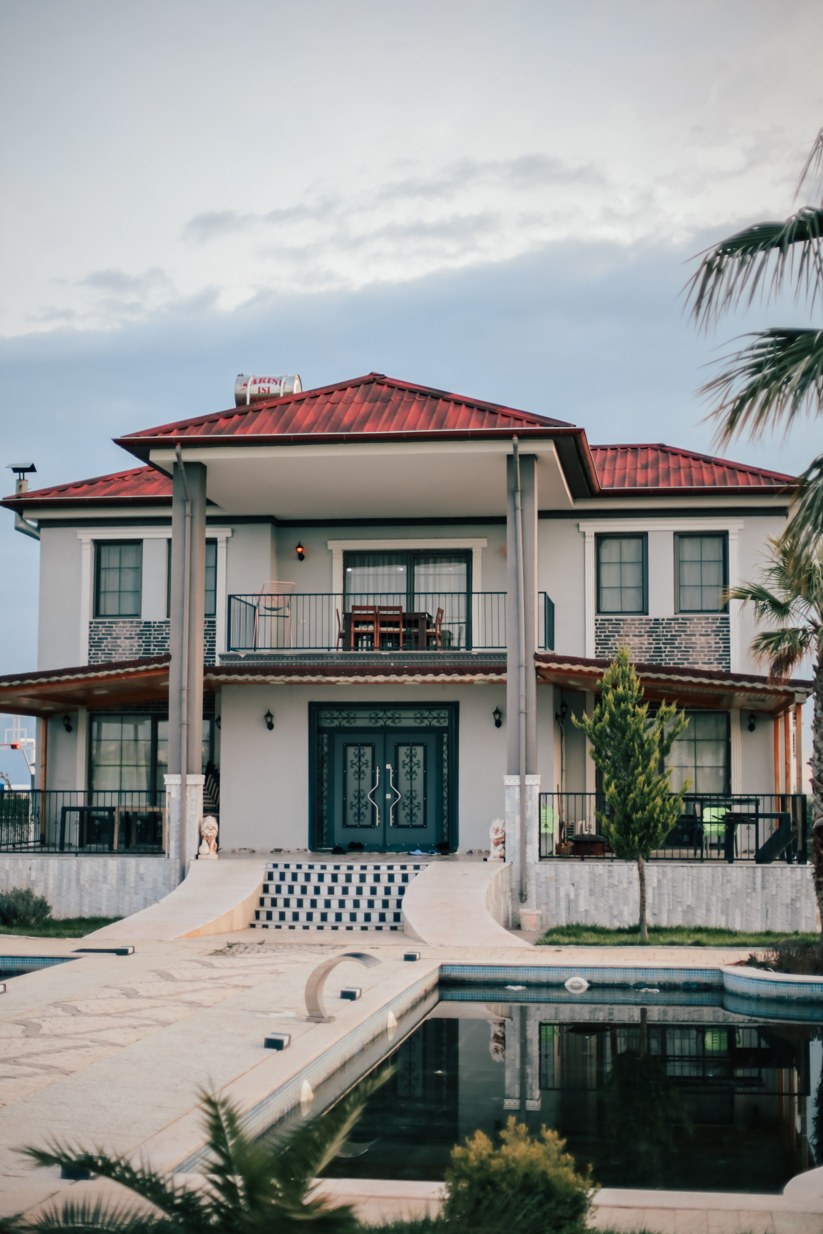 Two-storey white villa with red tile roof, balconies and pool in front