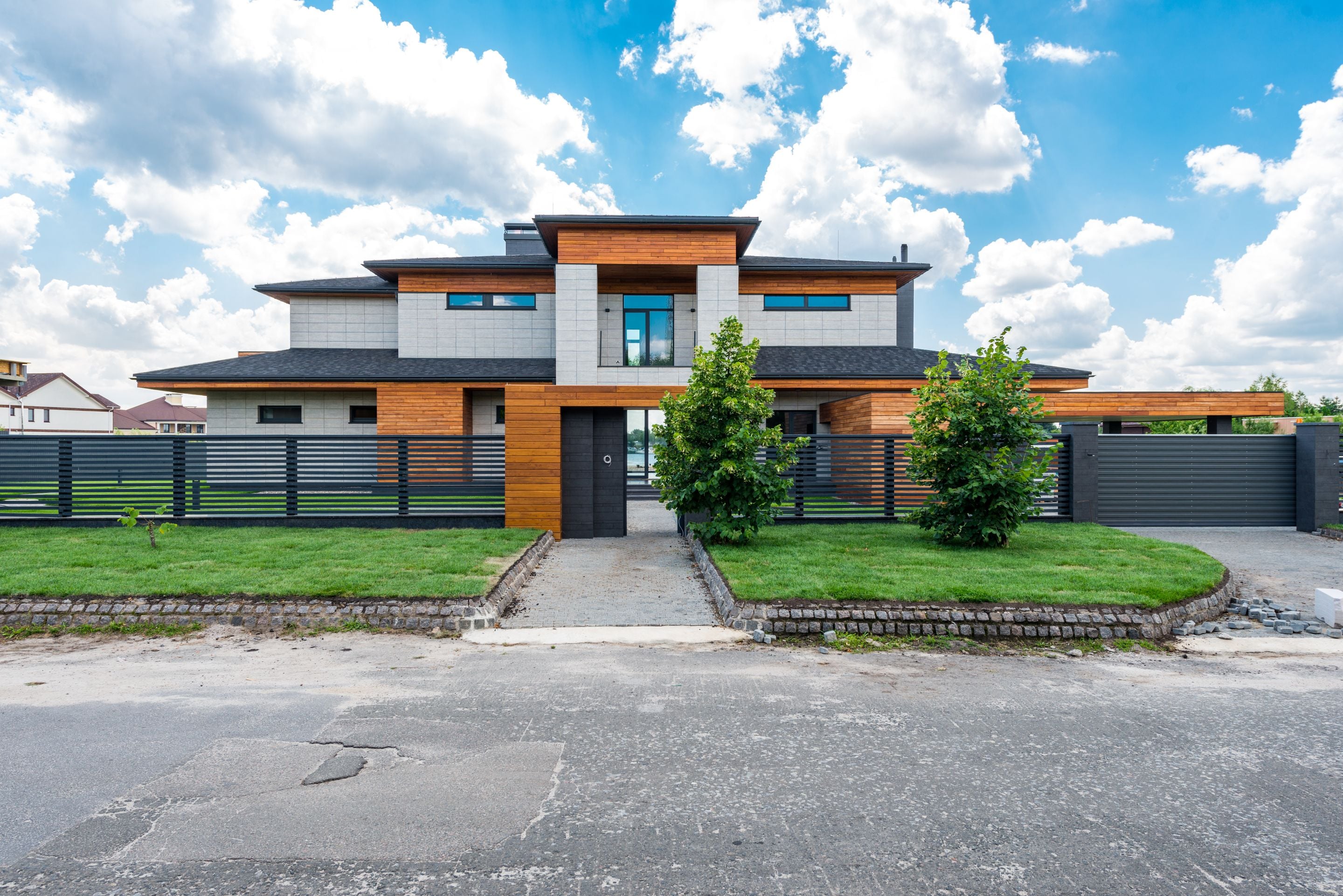 Fenced contemporary two-storey luxury house with lawn and driveway under cloudy blue sky