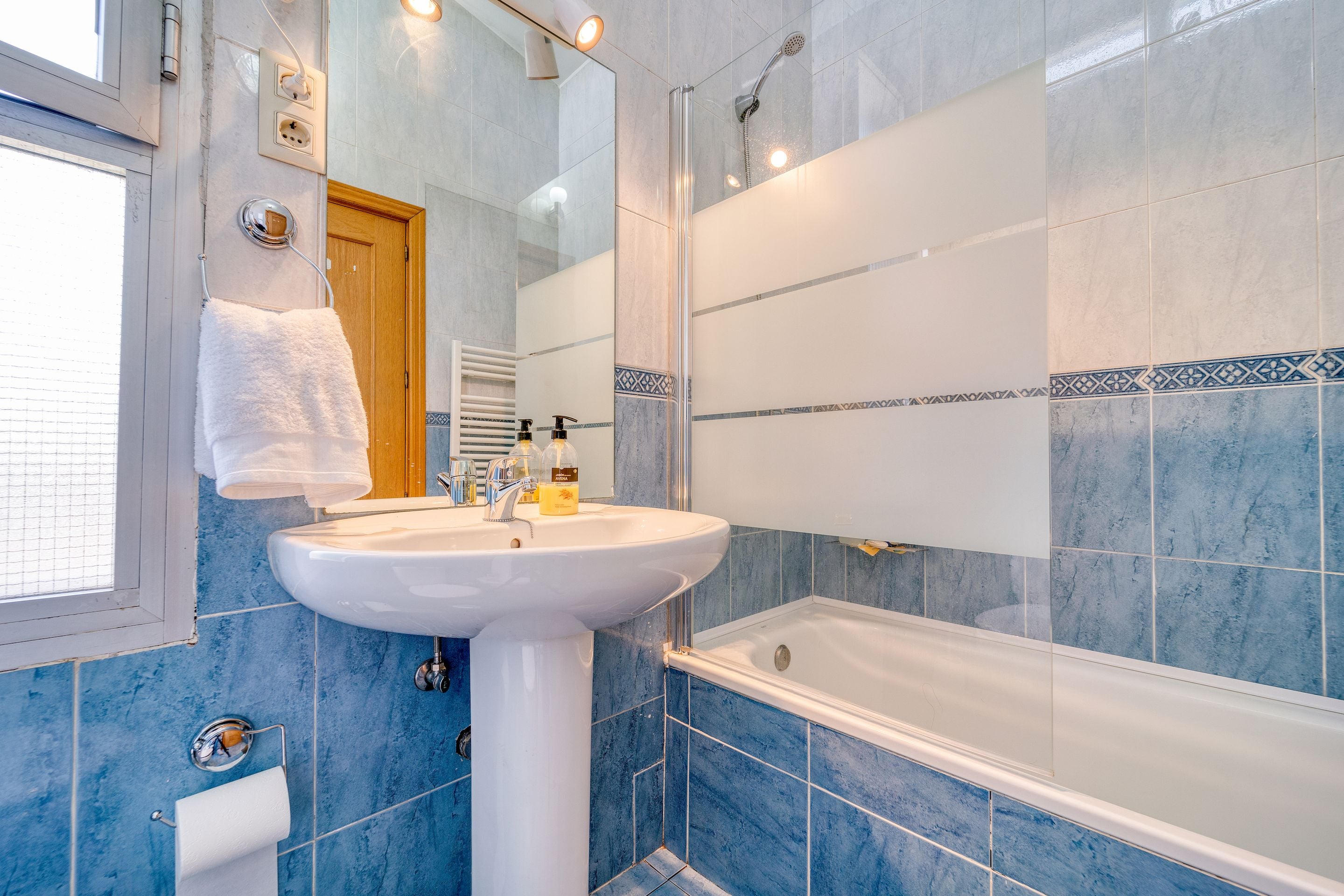 Bright bathroom with blue tiles, pedestal sink and bathtub