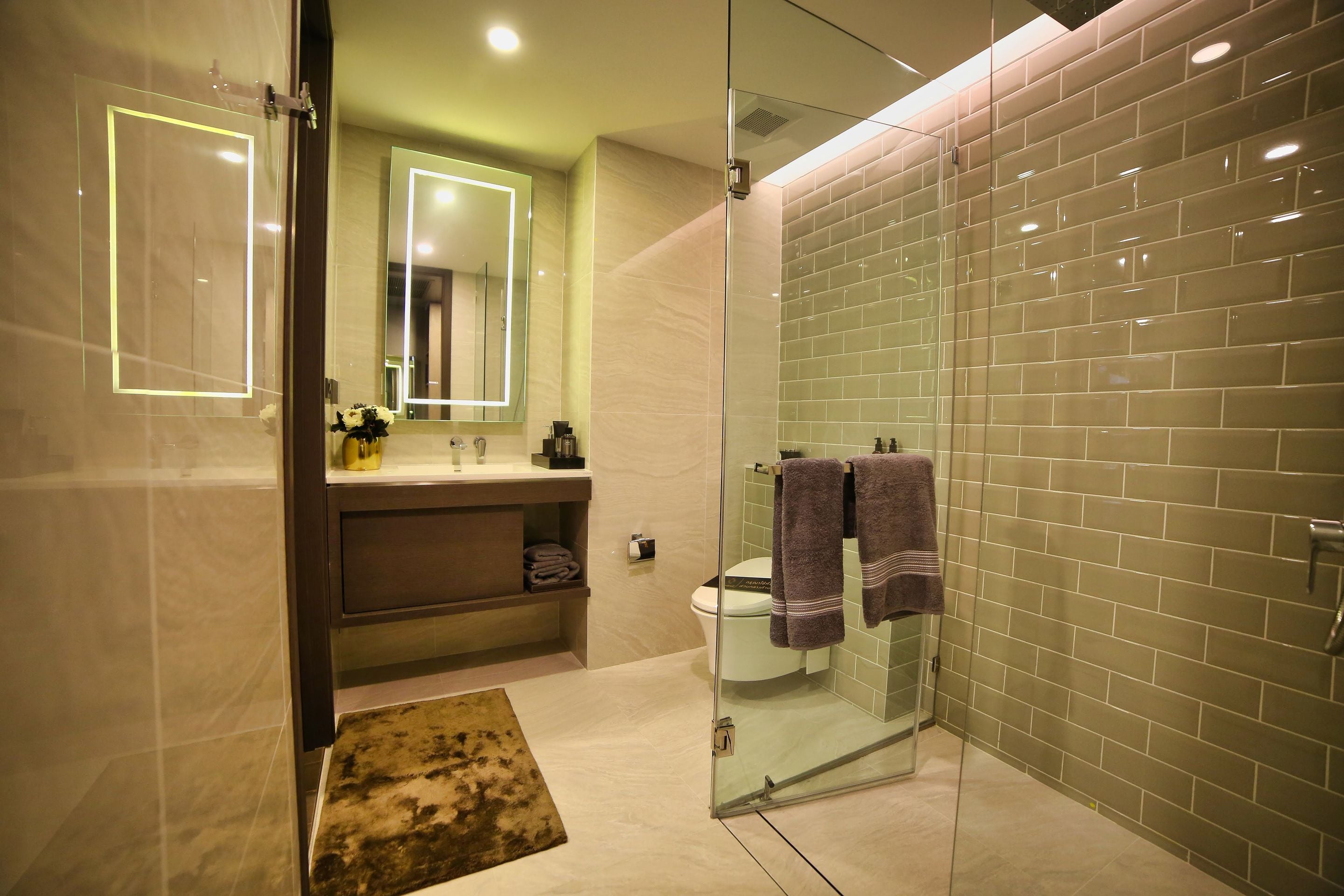 Luxury bathroom with glass shower, illuminated mirror and olive green tiled walls