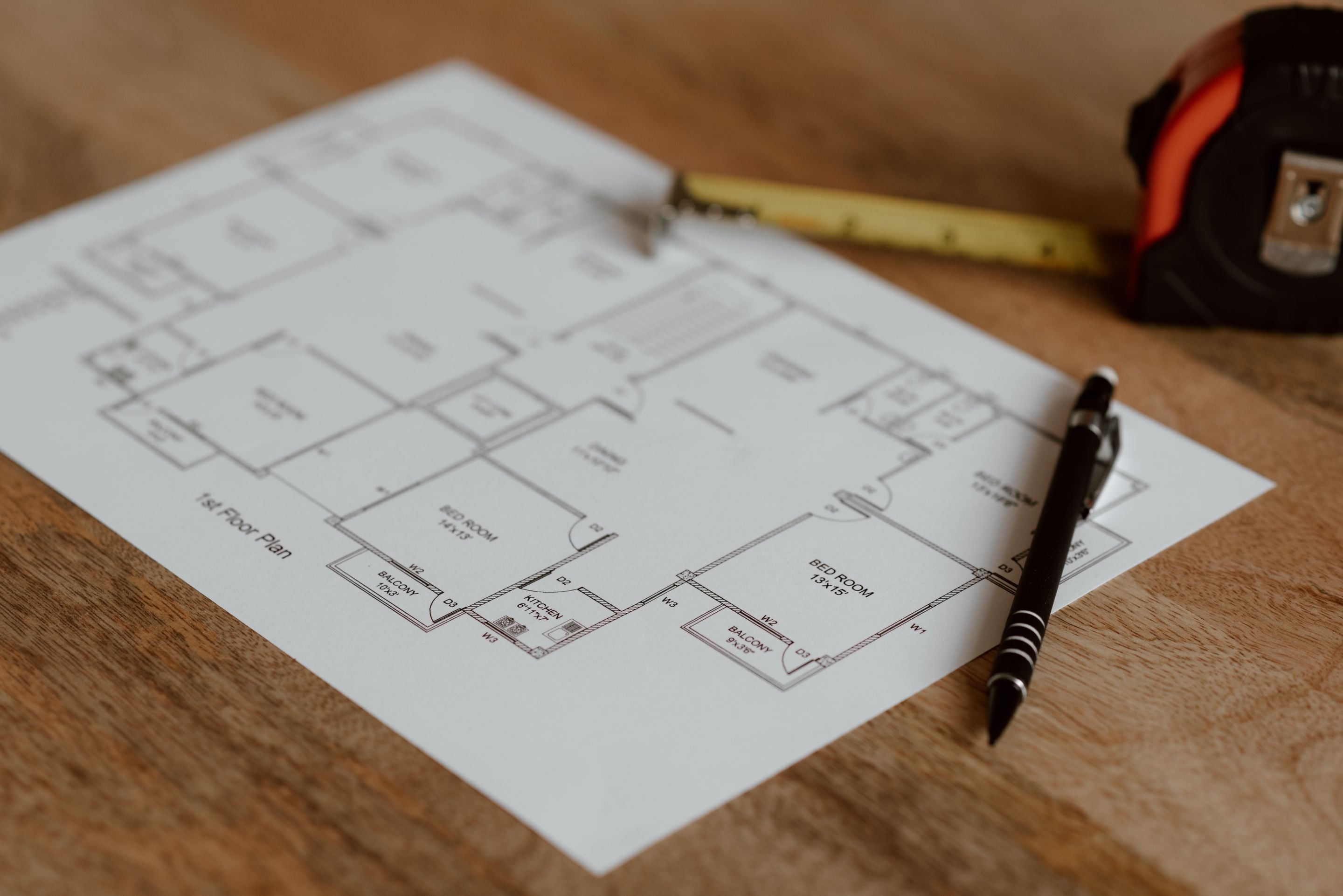 Printed house floor plan on a wooden desk beside a pen and tape measure