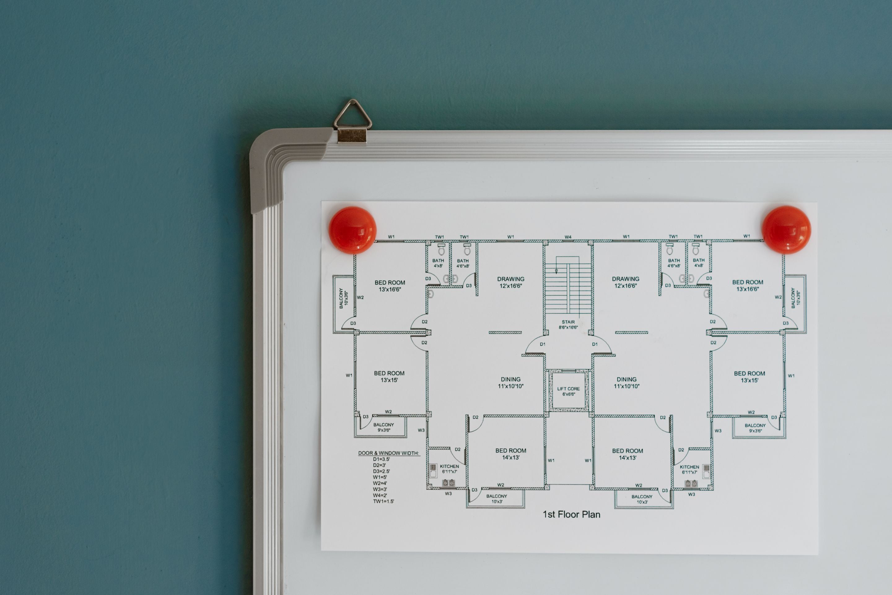 Black and white building floor plan pinned to a whiteboard with red magnets